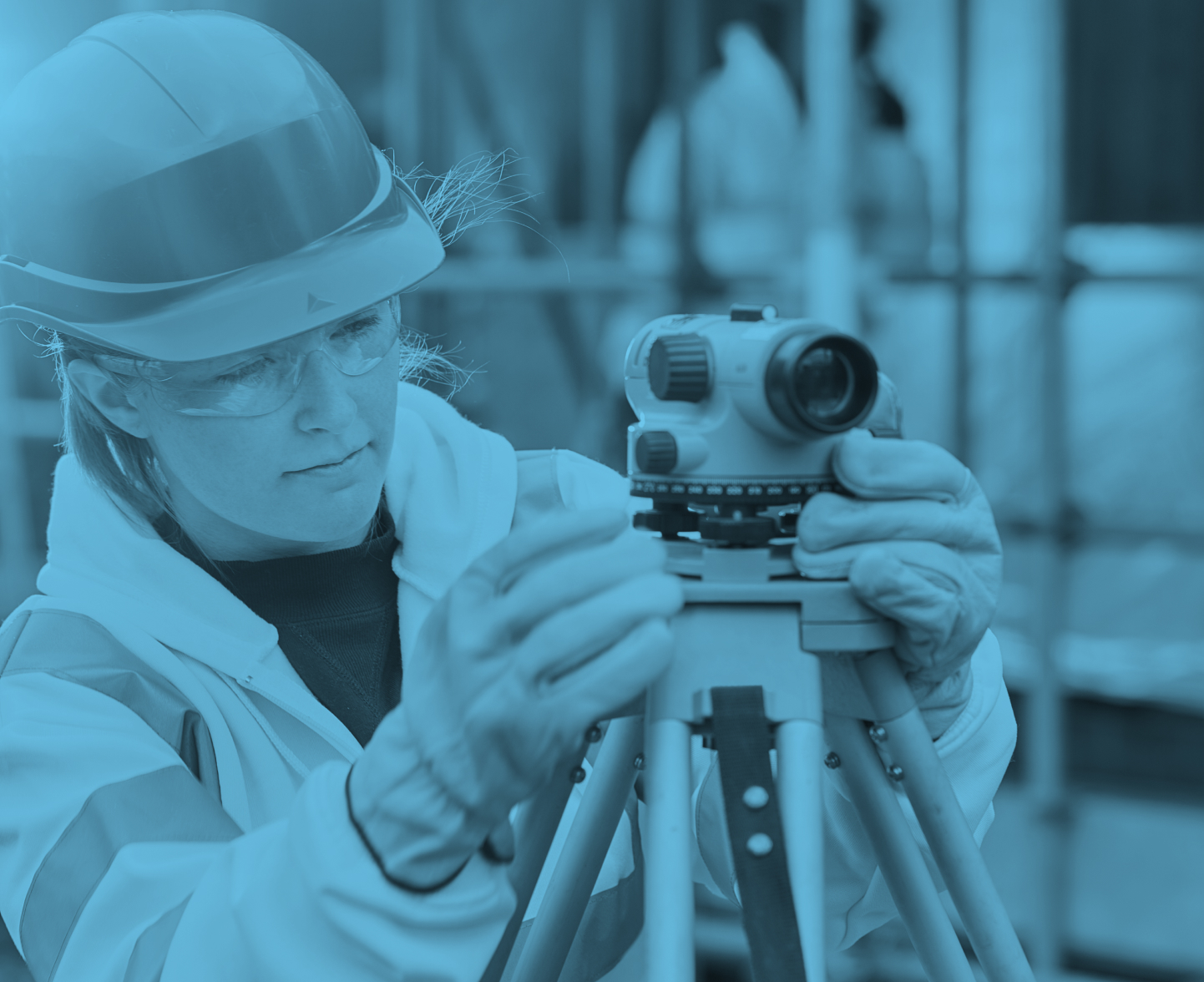 Woman wearing a hard hat on a construction site looking through a camera on a tripod