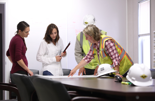 Group of people standing around a desk reviewing construction plans